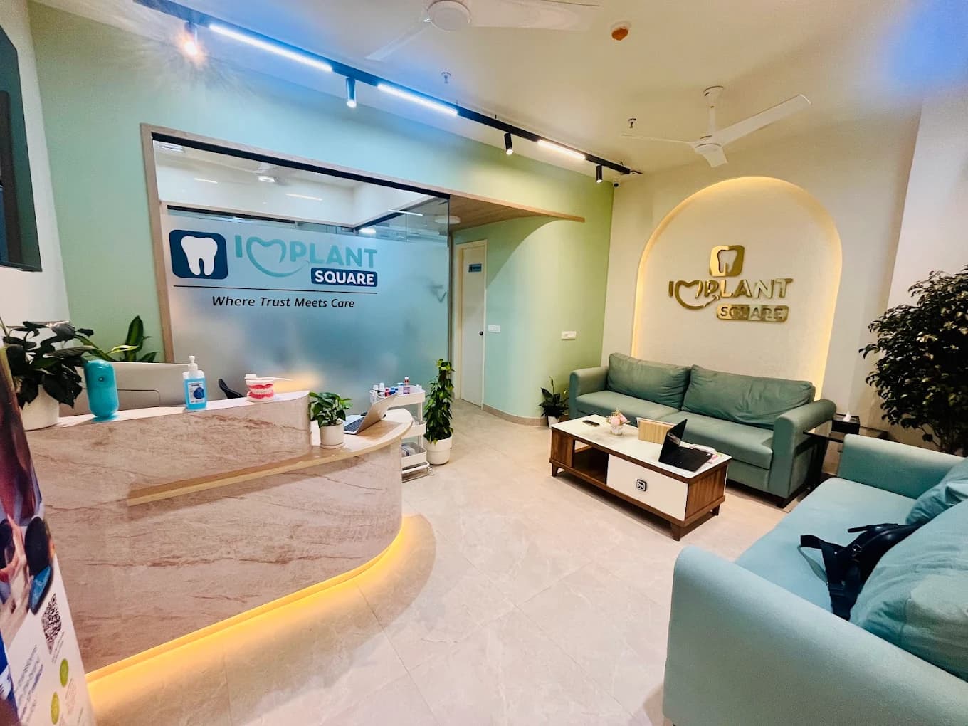 Implant Square reception and waiting area with curved marble desk, teal sofas, plants, and frosted glass showing the clinic logo and tagline Where Trust Meets Care.