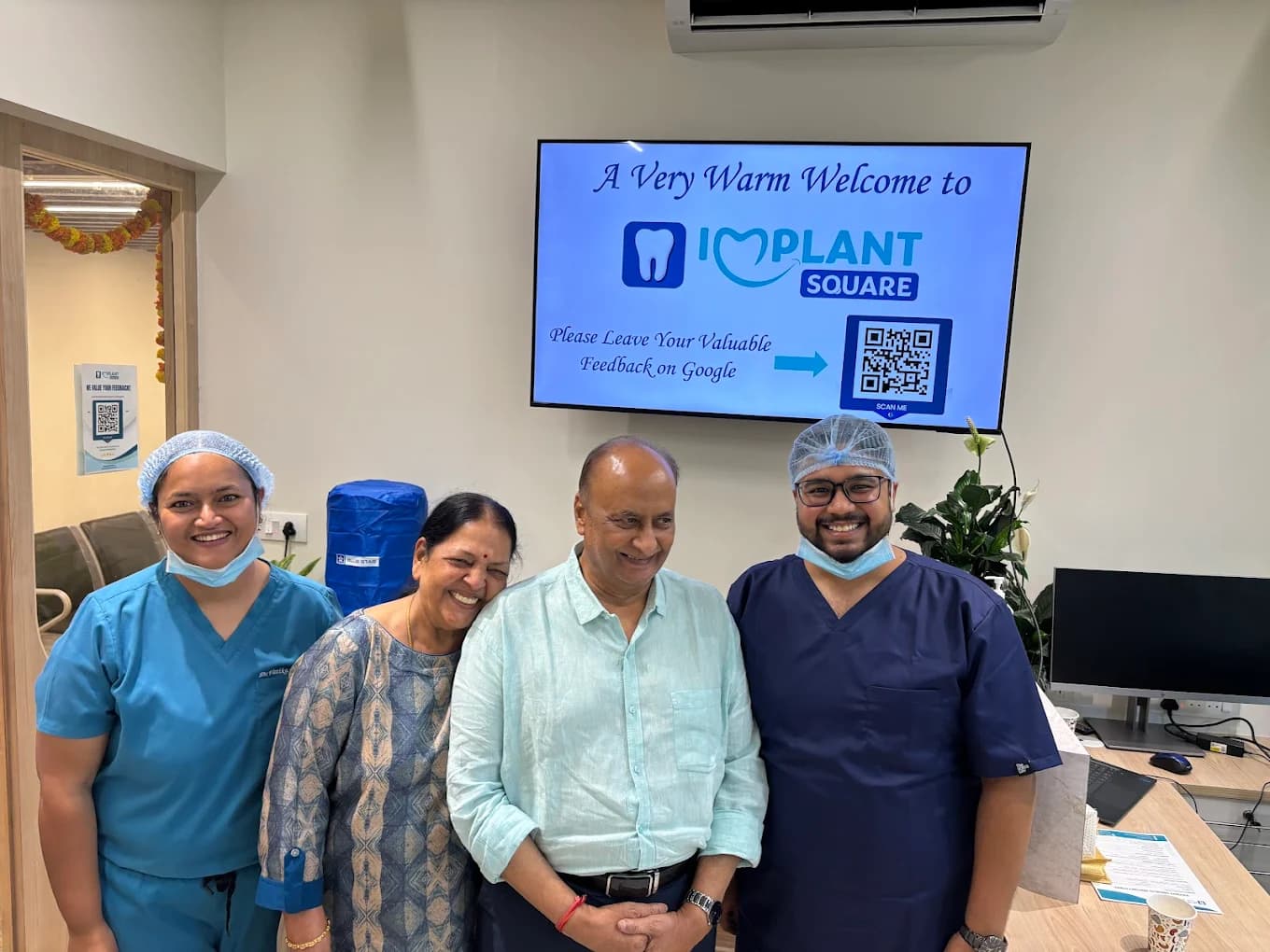 Implant Square staff in scrubs smiling with two patients in the reception area, welcome screen and Google review QR code visible on the wall.