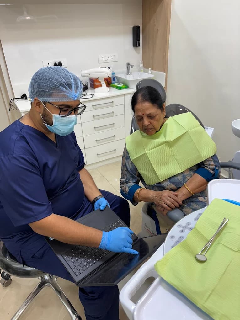 Dentist in protective gear showing a laptop screen to a seated patient in the dental chair during a consultation at Implant Square.